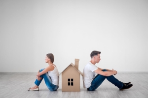 Coppia che si dà le spalle ed è divisa da una casa di cartone a simboleggiare le difficoltà di gestire un mutuo cointestato in caso di separazione.